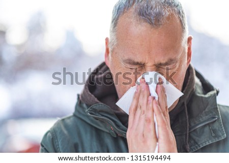 Sick Man Blowing his Nose. Closeup portrait of red eyed man holding tissue to his nose. Runny nose. A man holding a tissue and blowing his nose. Flu season, vaccination. 