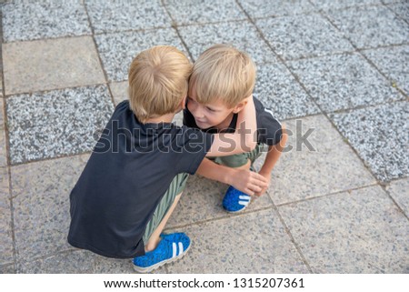 Two boys are sitting nearby. Older brother hugs younger. Friendship between brothers.