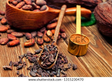 Cocoa beans in spoon, cocoa pods with green leaves, cacao powder in metal spoon and cocoa nibs in scoop on wooden background.