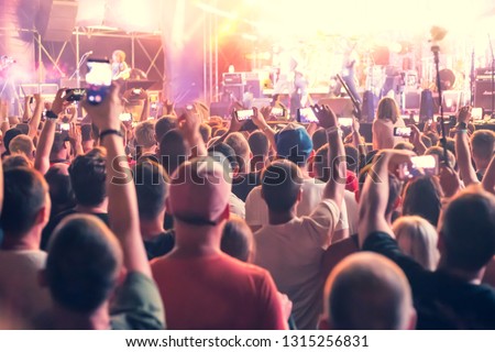 people standing with arms raised shoot a video on the phone at a street music show, blurred background Royalty-Free Stock Photo #1315256831