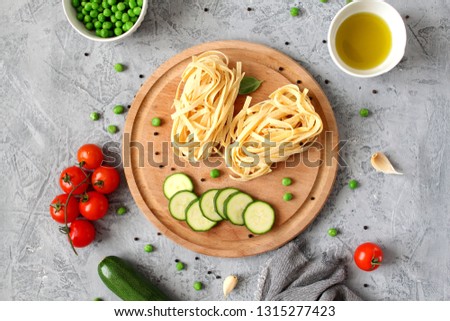 Dry pasta tagliatelle, zucchini, tomato, green beans, olive oil on light background. Top view. Vegetarian and vegan food. Diet food.