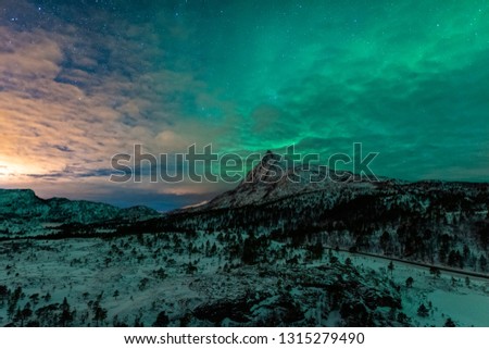 Northern light over the mountain "Littletinden" in northern Norway with some clouds and city light from left side. 