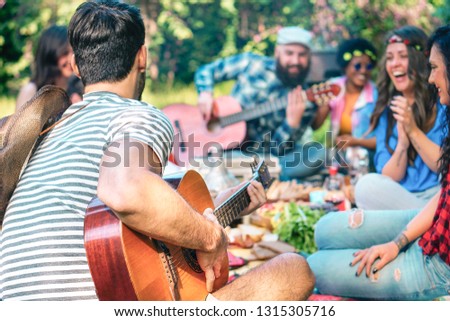 Young people doing picnic and playing guitar in park - Group of happy friends having fun during the weekend outdoor - Friendship, food and drink, funny activities and youth lifestyle concept 