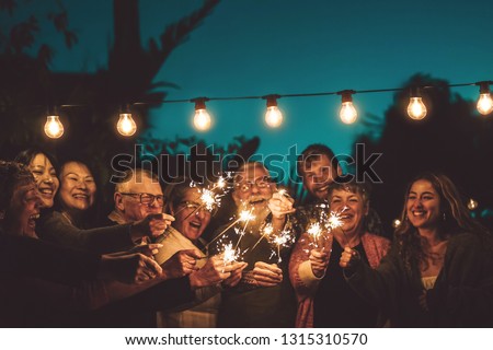 Happy family celebrating with sparkler at night party outdoor - Group of people with different ages and ethnicity having fun together outside - Friendship, eve and celebration concept
