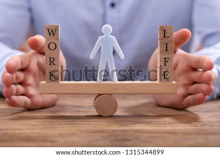 Human Figure Standing Between Work And Life Wooden Blocks On Seesaw Being Protected By Businessperson