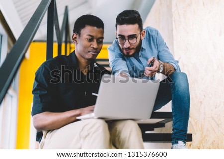 Two male friends making research of  content websites on netbook, multicultural men office employees sharing ideas while developing website on laptop computer. Caucasian and African American student
