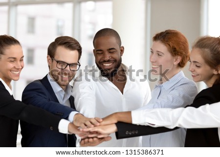 Six multinational millennial happy employees put join hands together in stack pile at group meeting, success celebration, corporate unity, help support promises in teamwork and team building concept Royalty-Free Stock Photo #1315386371