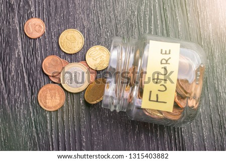 Open tilted glass jar with scattered euro coins with the inscription FUTURE on a black wooden table. The concept of savings for the prospect