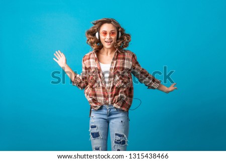 attractive smiling emotional woman jumping with funny crazy face expression in checkered shirt and jeans isolated on blue studio background, wearing pink sunglasses