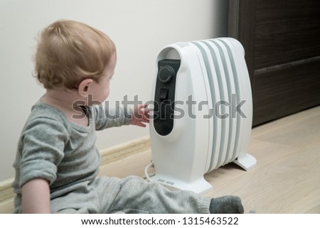 Little boy sitting on the floor near electric oil heater