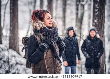 Portrait of a beautiful redhead girl with a backpack walking with his friends through a winter woods
