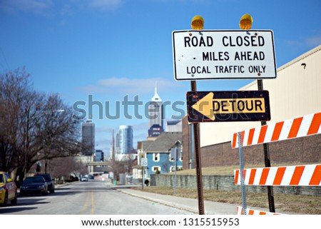 INDIANAPOLIS, IN - FEBRUARY 2019 : Road construction signs warn drivers of a closed road and a detour.  The Indianapolis skyline rises in the distance. 