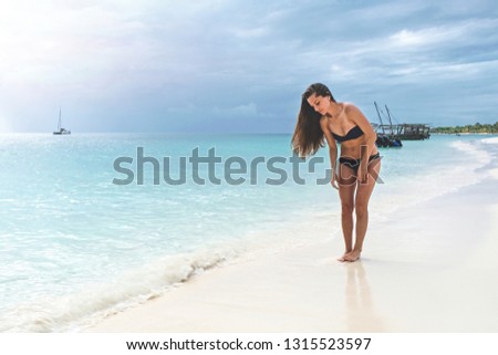 Attractive slim brown-haired woman in a bikini on a white sandy paradise beach Kendwa of Indian Ocean of Zanzibar island
