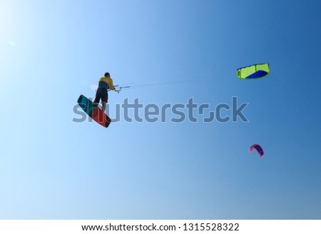 Professional kite boarding rider sportsman with kite in sky jumps high acrobatics kite boarding trick with massive kite loop in sky. Recreational activity, extreme active air sports, hobby and fun