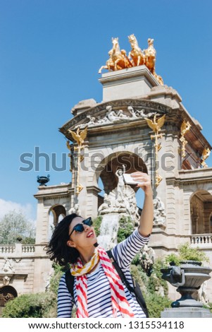 Pretty young woman taking selfie in front of the fountain of Parc de la Ciutadella in Barcelona, Spain