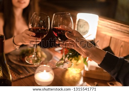 Hand of man and woman sitting in a dark restaurant by a table and holding glasses with red wine Royalty-Free Stock Photo #1315541771
