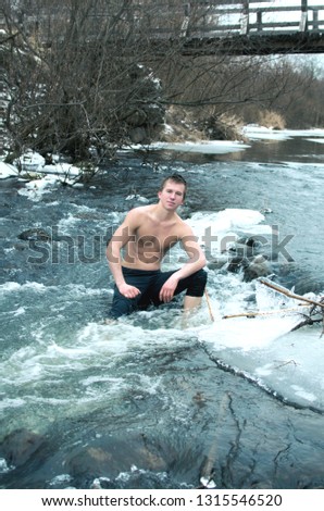 young man sits on the stones in the middle of the rapid current of icy river