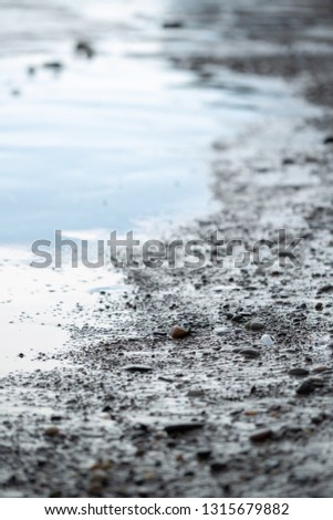 Side close up on a muddy beach with calm reflective water, in an abstract background