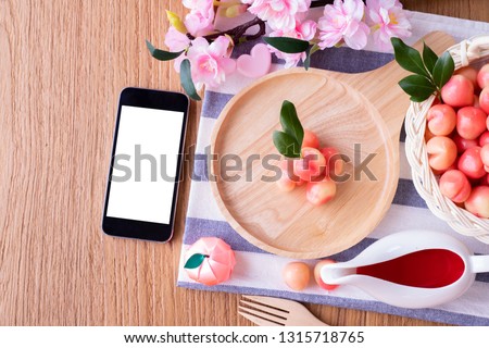 Wood table with blank screen on smart phone and Delectable imitation fruits, Fruit Shaped Mung Beans, Thai traditional dessert
