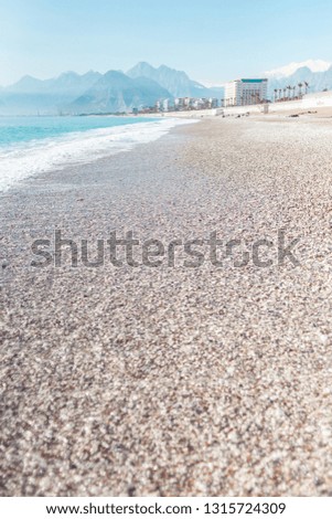 Turkish beach without people. Mediterranean Sea in Turkey. Ocean waves and coastal sand. Resort on the background of mountains and sky. Deserted beach.