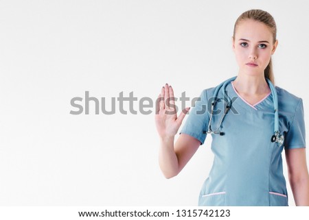 Woman doctor blonde young light gray background studio day beautiful one stethoscope pink purple lilac clothing protests hands forward and keeps feet free stop. Close up. Copy space left.