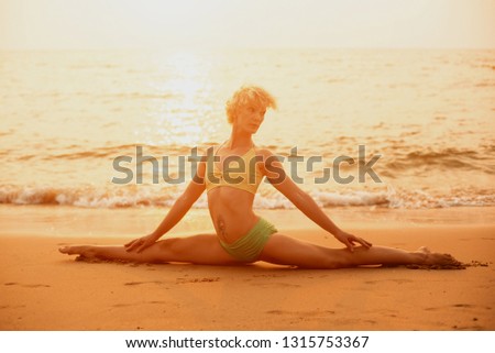 Beautiful young woman practic yoga at the beach. Early morning exercise. Palms background