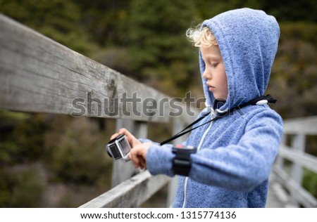 Young boy on a wooden bridge of a national park taking pictures with a action camera