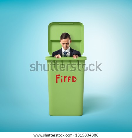 Young businessman in green trash bin with the red 'FIRED' sign on blue background. People and objects. Trash and garbage. Losing job.