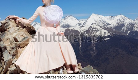 Beautiful young girl sitting in the snowy mountains in the spring, sunny weather in a fashionable luxurious peach long magnificent dress with a flower brooch