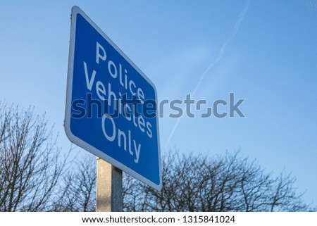 Blue Police vehicles onlye road traffic sign with tress and blue sky in the background.  Close up shot