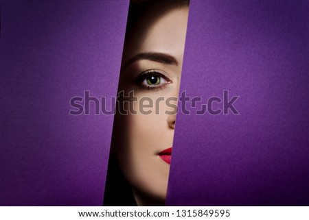 Eye of a girl in hole of paper purple background peeks into the lock well. Concept of advertising cosmetics bright makeup. 