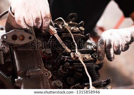 An old tractor repairman is working with a car engine in a garage, repairing the actual close-up pictures.