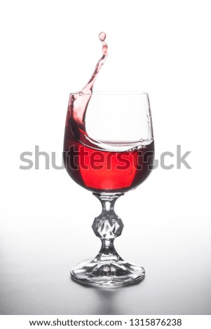 Drinks and beverages conception. Red wine splashing in wine glass with dynamic drops on light background.
