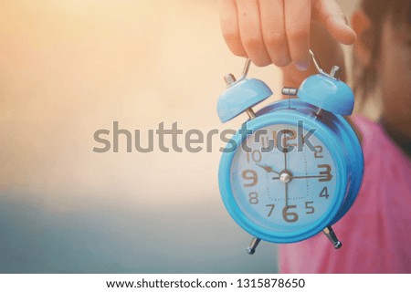close up kid hand holding blue alarm clock, nature copy space background for text, saving and manage time to success business concept, vintage tone