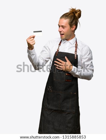 Barber man in an apron holding a credit card and surprised on isolated background