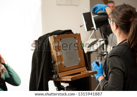 Photographer woman sets the ligths for portrait studio shooting. Large format camera in the foreground. 