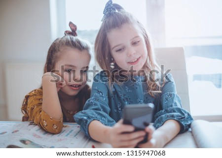 Let's ignore homework, let's take a picture. Two little school girls taking a self portrait. Focus on foreground Close up.