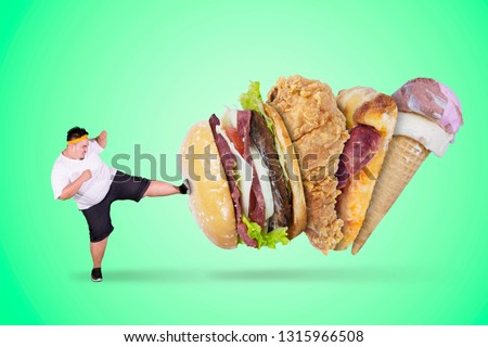 Picture of angry fat man kicking fast foods while wearing sportswear in the studio with green screen