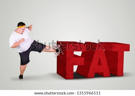 Picture of angry fat man kicking fat word in the studio while wearing sportswear