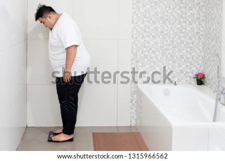 Picture of young fat man checking his weight while standing on the scale. Shot in the bathroom