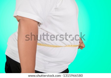 Close up of an unknown obese man measuring his oversize belly with a measure tape in the studio