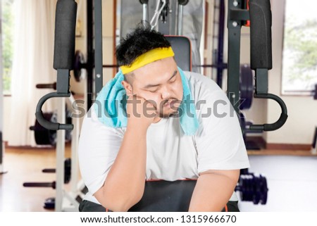 Picture of young obese man looks lazy while sleeping on the exercise machine. Shot in the gym center
