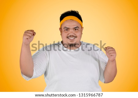 Picture of happy fat man expressing his success to lose weight while standing with yellow background