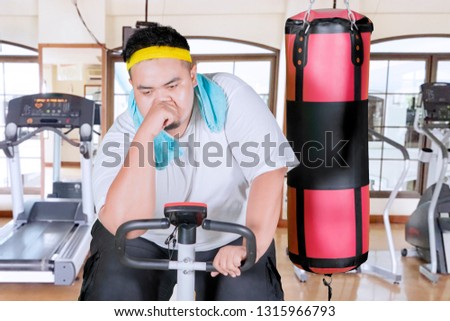 Image of exhausted fat man looks sweaty after doing workout with exercise bike in the gym center