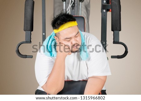 Picture of young fat man looks asleep while sitting on the exercise machine