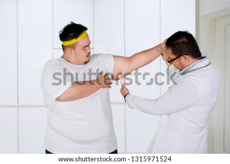 Picture of a male doctor measuring fat arm layer of his patient by using calipers. Shot at the clinic