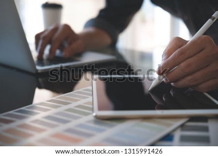 Website designer, graphic designer  creating project on mobile apps with stylus pen on digital tablet screen. Business man working on laptop and tablet computer with color swatch sample in office