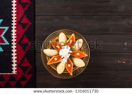 Golden tray with shekerbura and pakhlava for Novruz, Azerbaijan traditional pastry for spring equinox and Persian Nowruz, Navruz new year celebration on dark brown wooden background with rug carpet