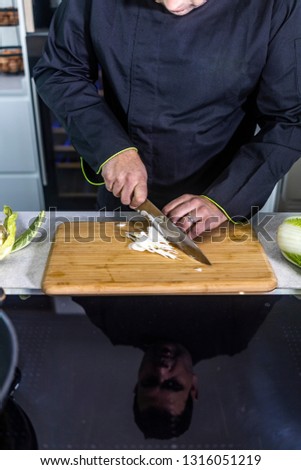 Chef cutting onion on a wooden board