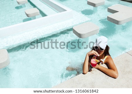 Girl relaxing and drinking watermelon cocktail in the hotel pool. Healthy fruit summer diet. Tropical beach lifestyle.